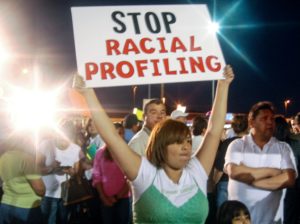 Una manifestante sostiene un letrero que lee: "Alto al perfil racial" como protesta contra una redada de inmigración en el Condado Maricopa en Arizona. Foto: Eduardo Barraza | Barriozona Magazine © 2011