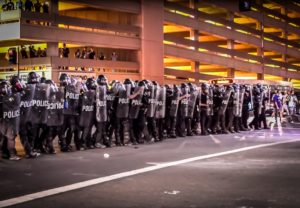 A battalion of Phoenix Police officers in riot gear advance toward protestors who clash with them after the political rally where President Donald Trump spoke to supporters. Photo: Jon Hernandez | Barriozona Magazine © 2017
