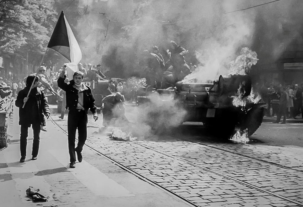 Imagen captada durante la invasión soviética de Checoslovaquia en 1968, en la que se observa a jóvenes manifestantes checoslovacos llevando su bandera nacional junto a un tanque en llamas en la ciudad de Praga. Foto: Dominio Público