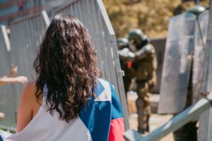 Una joven activista envuelta en una bandera chilena frente a la policía antidisturbios en una manifestación en 2020. Muchos jóvenes están liderando movimientos e impulsando el cambio social y ambiental en países de América Latina. Foto: David Knox | Unsplash