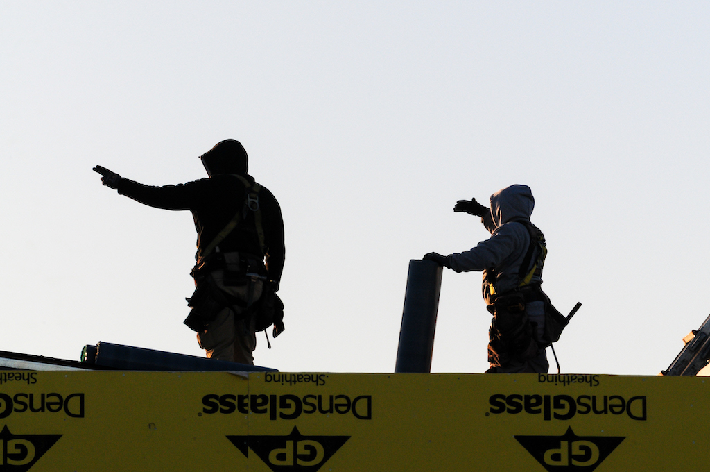 Dos trabajadores de la construcción instalan rollos de contrapiso para techo en una estructura en edificación en el condado de Maricopa, Arizona. No son terroristas ni espías; son inmigrantes construyendo Estados Unidos, un contraste evidente con la narrativa alarmista de la orden ejecutiva que alude a una supuesta "invasión". Su esfuerzo simboliza el papel esencial de la mano de obra inmigrante en el desarrollo económico del país. Foto: Eduardo Barraza | Barriozona Magazine © 2025